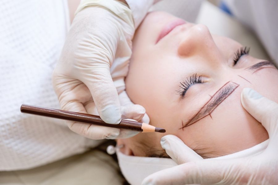 Close-up of the hand of a beauty master woman sketching a new eyebrow shape to a young female client. Concept of eyebrow tattoo and microblading